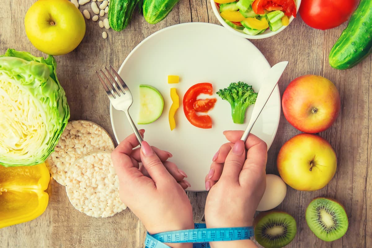 Manos atadas a cinta métrica delante de un plato de dieta